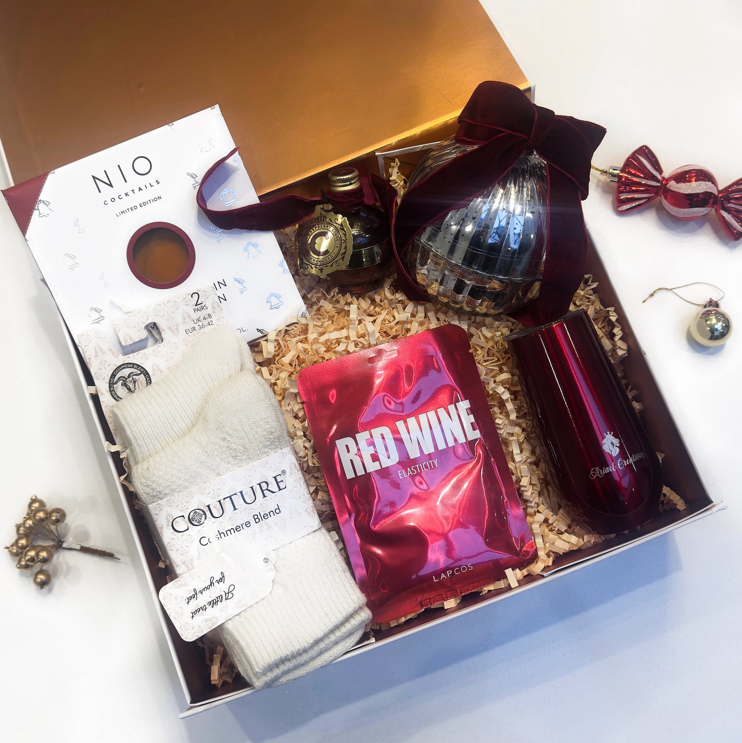Gift set with red wine, clothing, and decorative items on a white surface