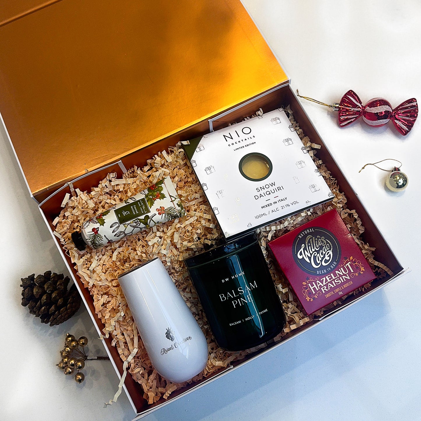 Gift box with tea items including a white mug, black teapot, and a box of tea on a light background.