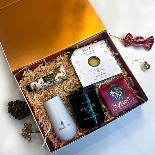 Gift box with tea items including a white mug, black teapot, and a box of tea on a light background.